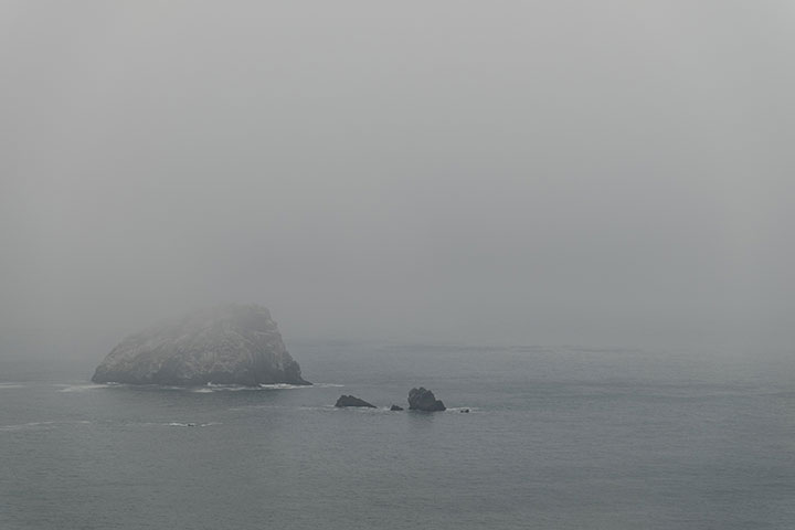 view of ocean with rock formation in the fog
